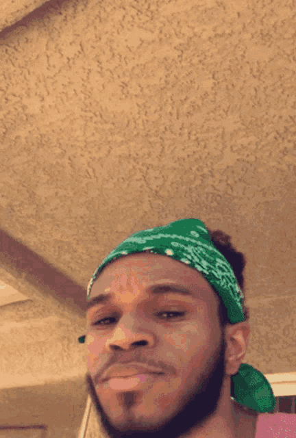 a man with a beard wearing a green bandana and a pink shirt