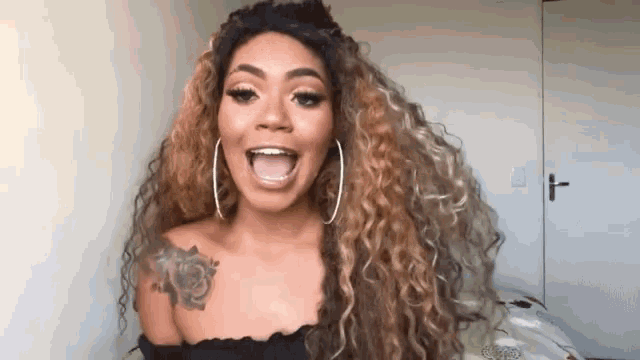 a woman with long curly hair and hoop earrings is smiling with her mouth open