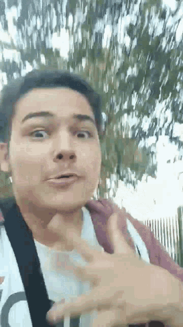 a young man is making a funny face while standing in front of a tree