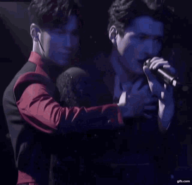 two men are hugging each other while one sings into a microphone .