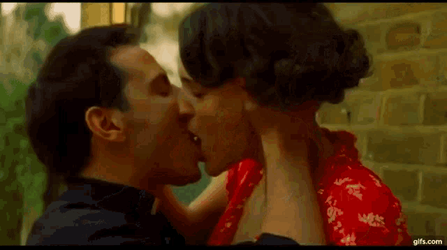 a man and a woman are kissing each other in front of a brick wall .