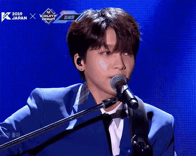a man singing into a microphone in front of a screen that says " 2019 japan "