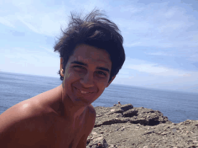 a shirtless man is smiling in front of a body of water