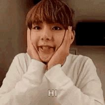 a young boy is making a funny face with his hands on his face and says hi .