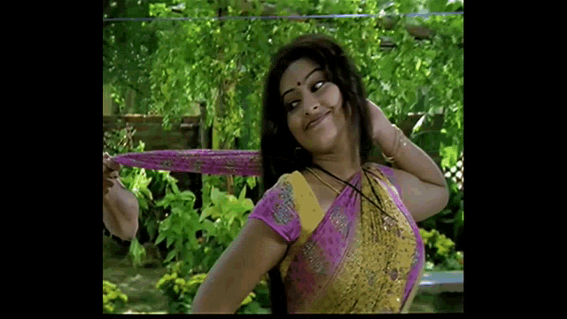 a woman in a pink and yellow top is smiling and holding her hair
