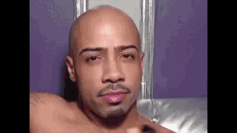 a bald man with a beard is laying on a couch .