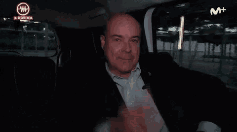 a man is sitting in the back seat of a car making a stop gesture with his hand .
