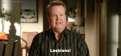 a man in a striped shirt is standing in a living room and says `` lesbians '' .