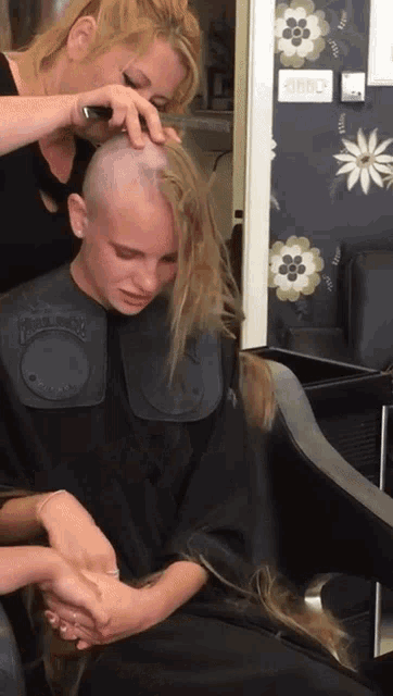 a woman is getting her hair cut by a woman with a shaved head