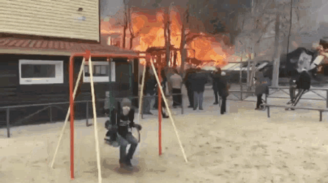a man is sitting on a swing in front of a burning building .