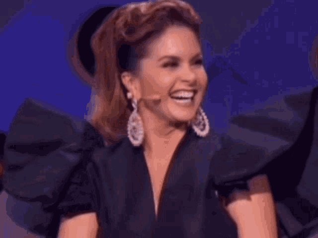 a woman wearing a black top and earrings is laughing and smiling .