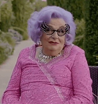 a woman with purple hair and glasses is wearing a pink dress and sitting on a bench .