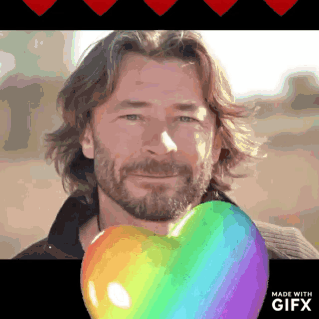 a man with a beard is holding a rainbow heart in front of him