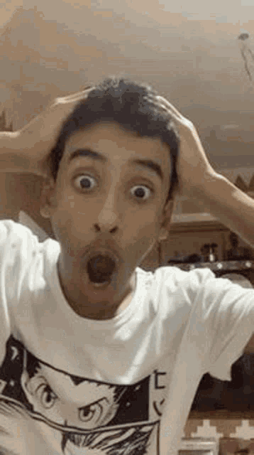 a young man is making a surprised face while holding his head with his hands .