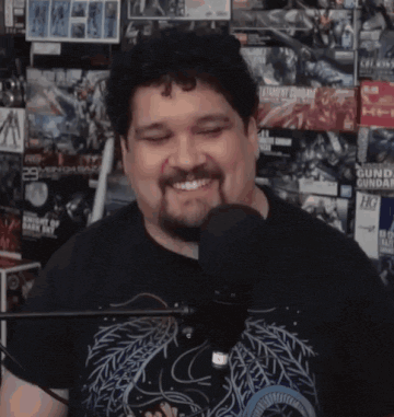 a man with a beard is smiling in front of a microphone while wearing a black shirt that says gundam