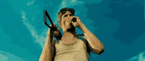 a man in a tank top and goggles is holding a gun .