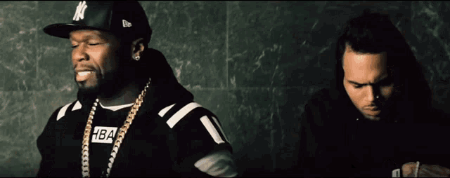 a man wearing a hba sweatshirt sits next to a man wearing a ny hat