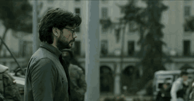 a man with glasses and a beard is standing in front of a building in a city .