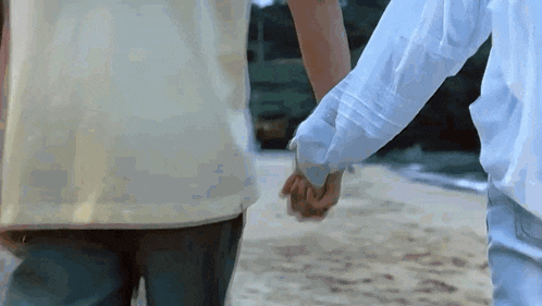 a man and a woman are holding hands on the beach .