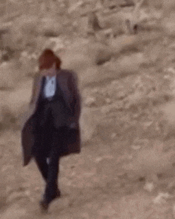 a woman in a coat is walking down a dirt road .