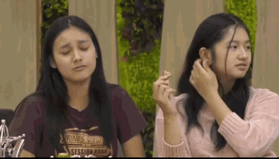 two young women are sitting next to each other and one of them is eating a piece of food .