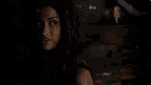 a close up of a woman 's face in the dark with a brick wall in the background .