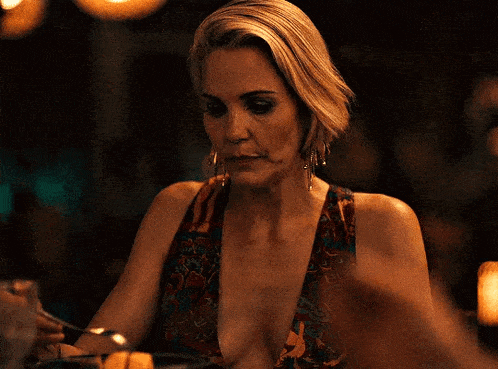 a woman in a plunging neckline dress is sitting at a table with a fork in her hand .