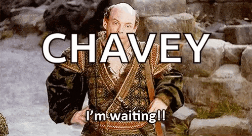 a bald man in a costume is standing in front of a stone wall and says chavey i 'm waiting