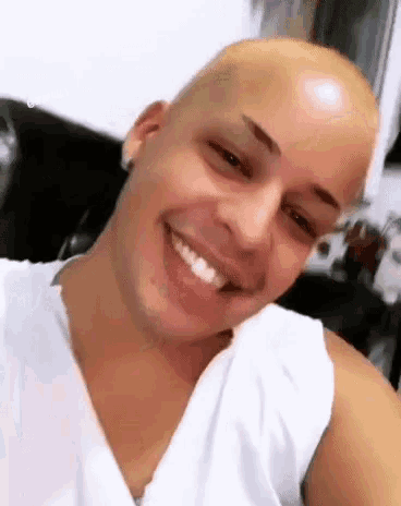 a man with a bald head is smiling and wearing a white shirt .
