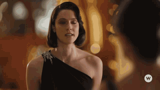 a woman in a black dress with a white w logo on her shoulder