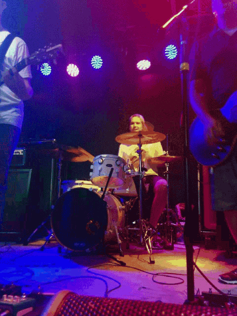 a man playing drums and a man playing a guitar on a stage with purple lights