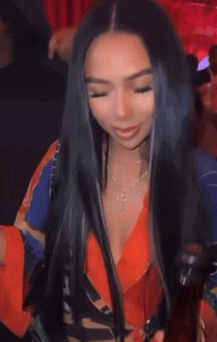 a woman with long black hair is holding a bottle of beer in a crowded room .