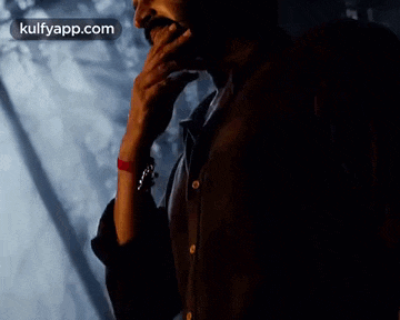 a man is holding his hand to his chin and looking at something in the dark .