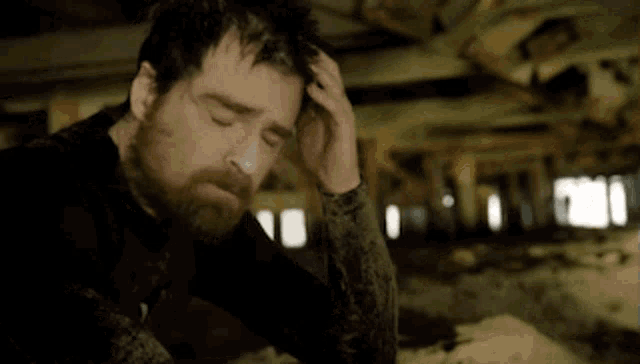 a man with a beard is holding his head while sitting under a bridge .
