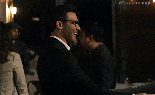 a man in a suit and glasses is laughing in front of a sign that says cwsupermangin