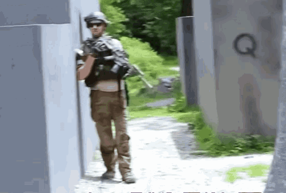 a man in a military uniform is standing next to a wall with a letter q painted on it .