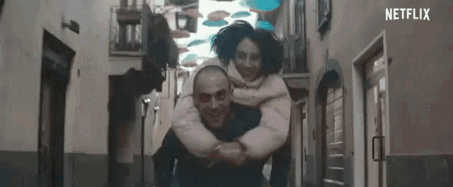 a man is carrying a little girl on his shoulders down a narrow street .