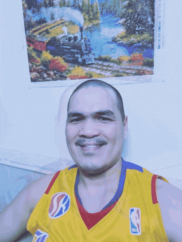 a man wearing a yellow nba jersey smiles in front of a painting of a train
