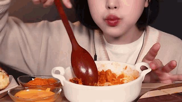 a woman is eating food with a wooden spoon in a bowl .