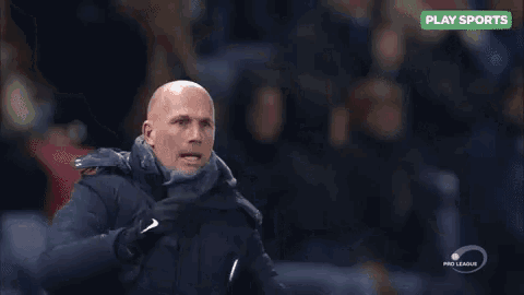 a bald man in a blue jacket and scarf stands in front of a sign that says play sports