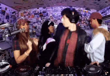 a group of people are dancing in front of a microphone in a room with stickers on the wall