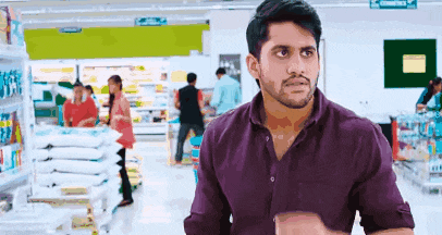 a man in a purple shirt is standing in a grocery store looking at something .