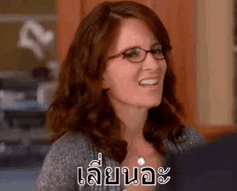 a woman wearing glasses and a sweater is smiling and making a funny face .
