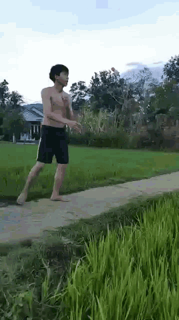 a shirtless man is walking down a path in a field of grass .