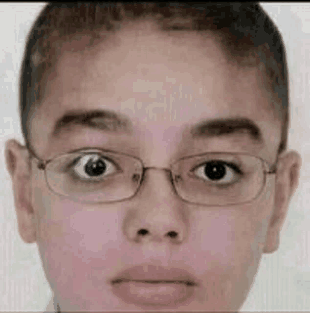a young boy wearing glasses is looking at the camera with a sad look on his face .