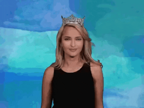 a woman wearing a crown and a black tank top is waving her hand .