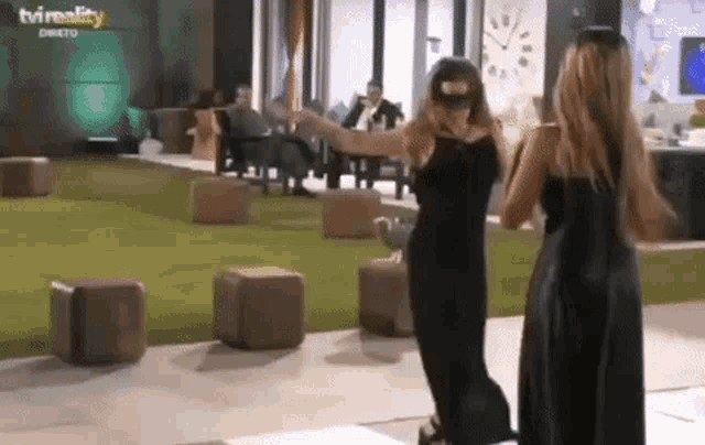 two women in black dresses are standing next to each other in a room with a clock on the wall .