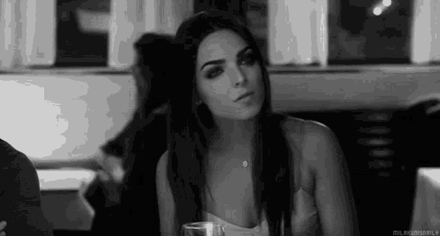 a black and white photo of a woman sitting at a table in a restaurant with a glass of wine .