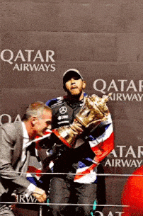a man is kissing a man on the cheek while holding a trophy in front of a wall .