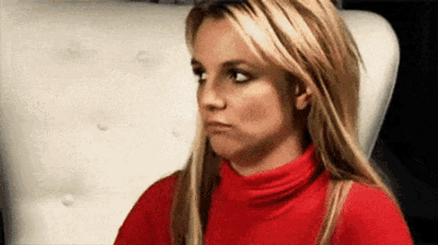 britney spears is wearing a red turtleneck and making a funny face .